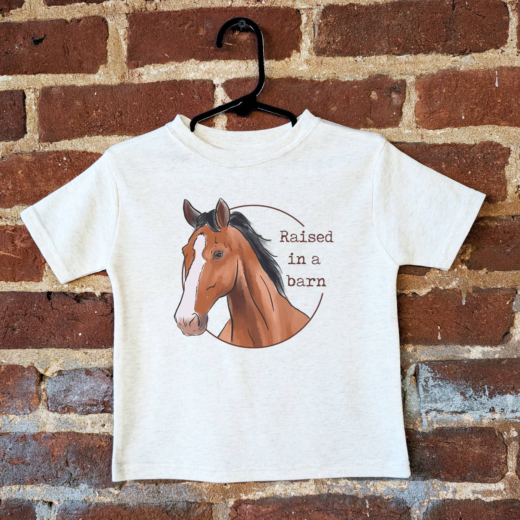 PuShort sleeve tshirt in white with graphic of a horse and text "Raised in a barn"