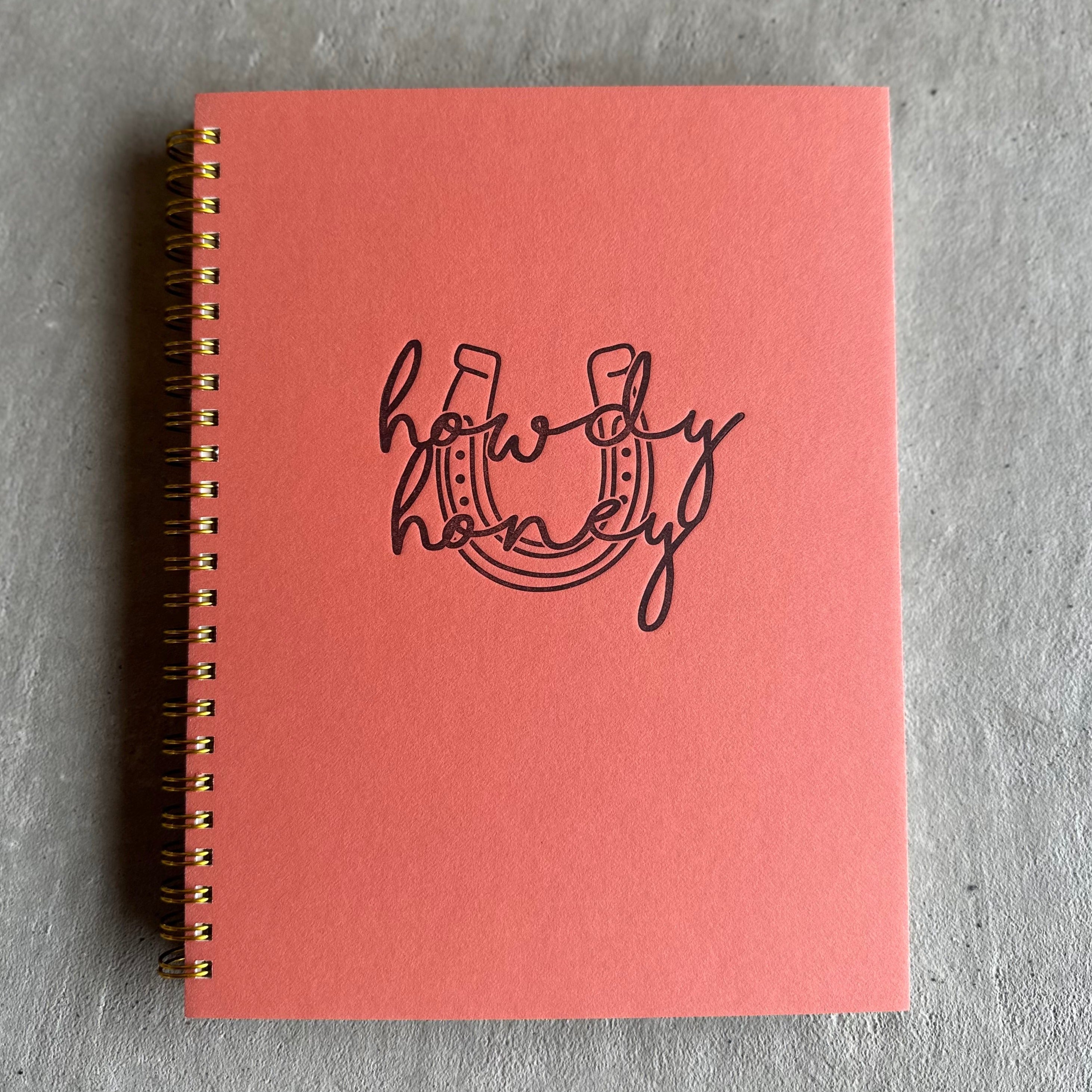 Pink wire-bound notebook with debossed text "Howdy Honey" with a horseshoe behind text