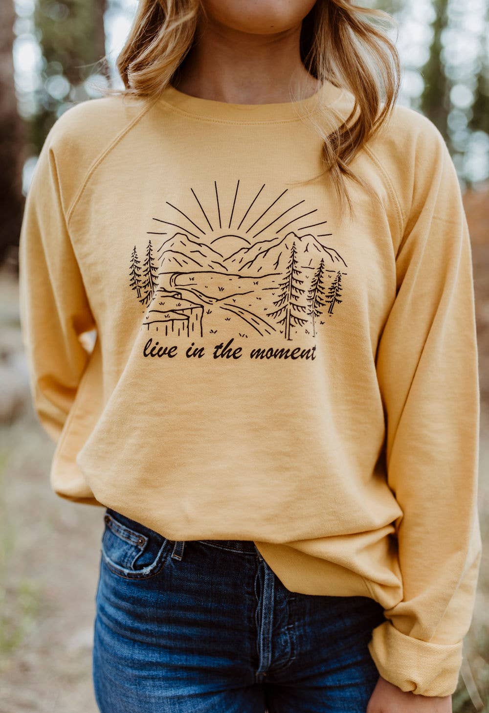 Yellow pullover. Mountain landscape in black linework, with text "live in the moment" under graphic.