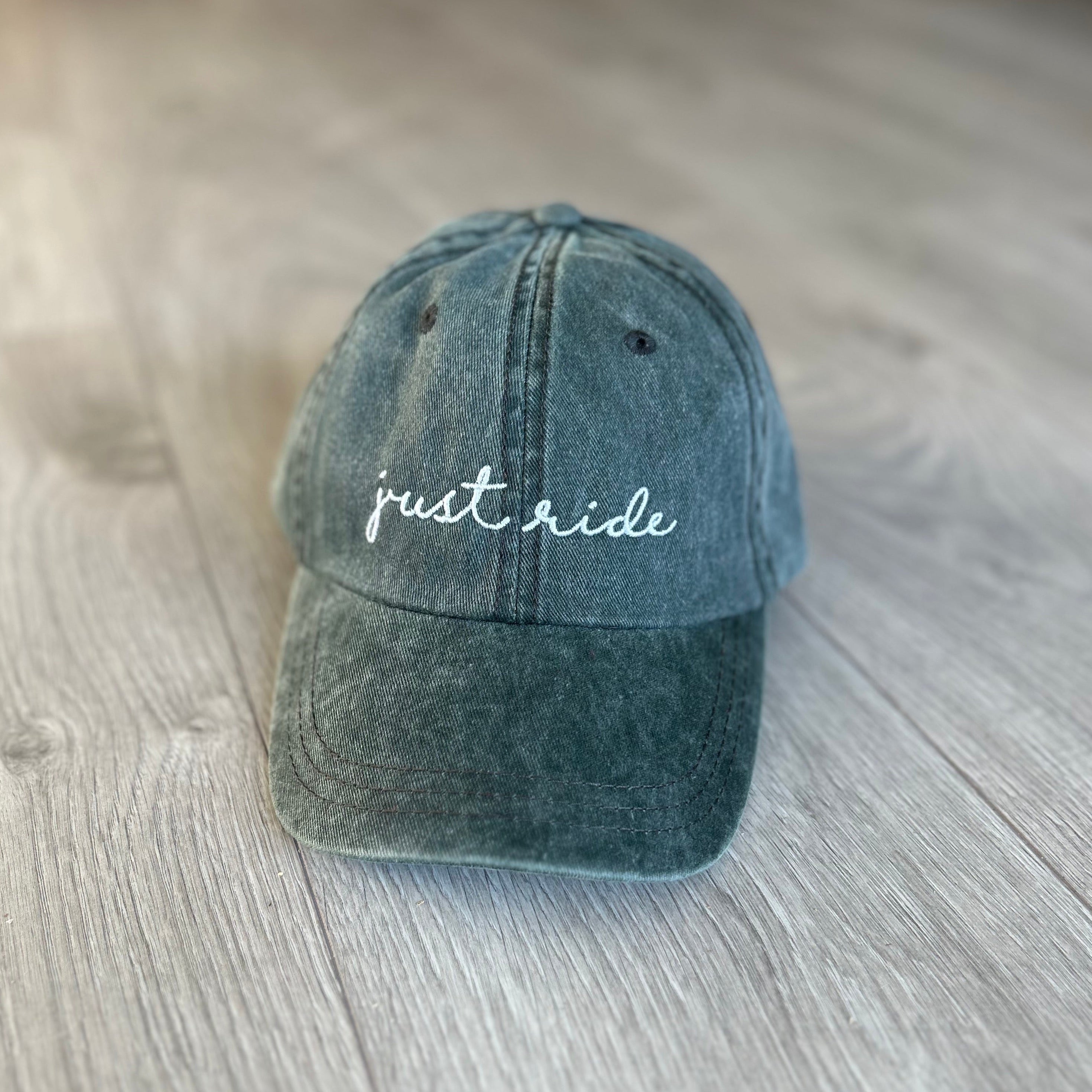 Green baseball cap with embroidered text "Just Ride" in white